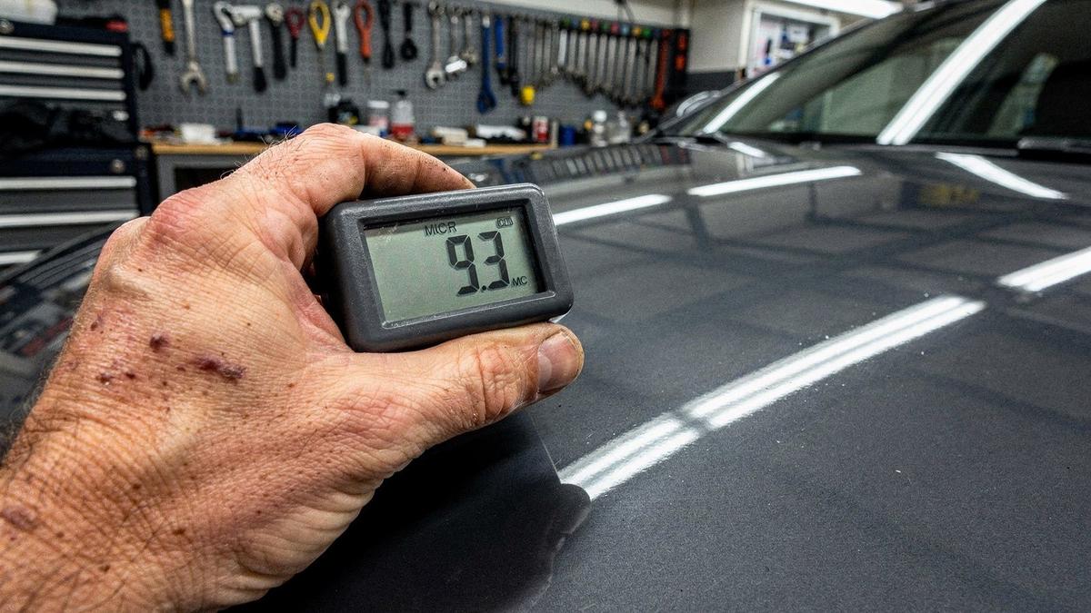 Digital paint depth gauge resting on a car hood during measurement